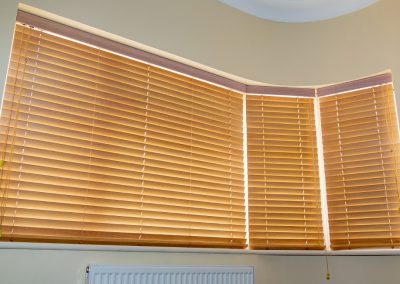 Three wooden venetian blinds covering a curved window