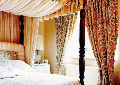 Full length pleated curtains, with rope-style tie backs and matching pelmet on a four-poster bed