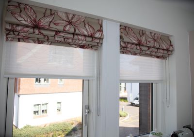 Pair of roman blinds in red floral fabric, with pleated blinds behind for extra light protection